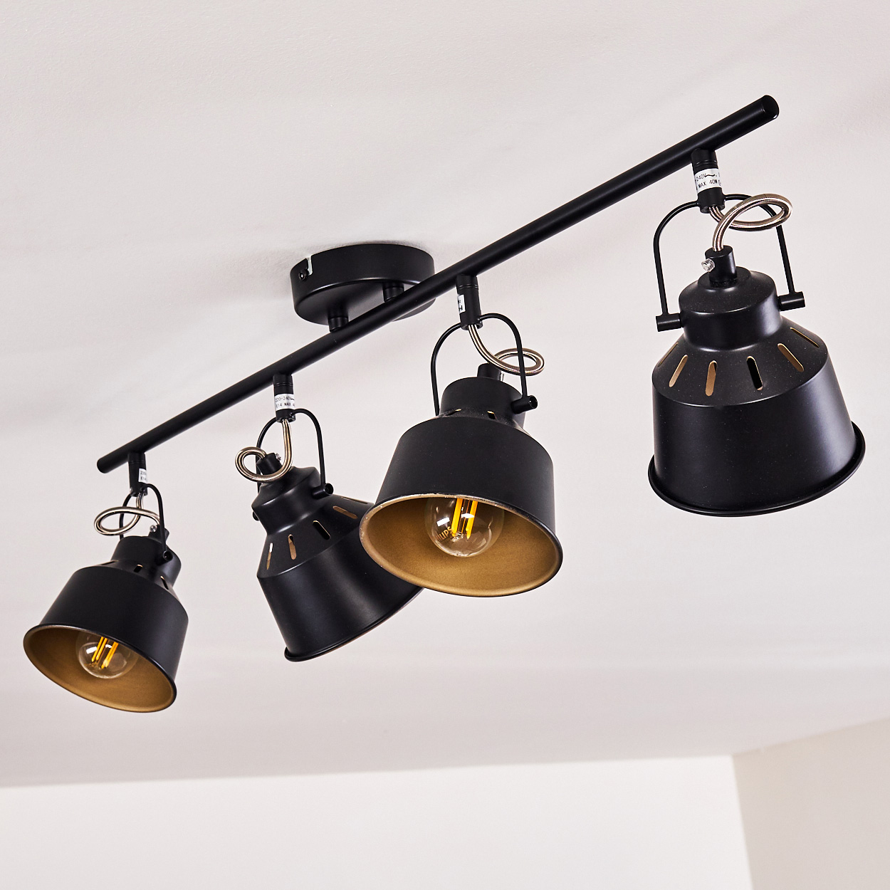 Schwarze Deckenleuchte mit vier Lampenschirmen und goldenem Innenleben.