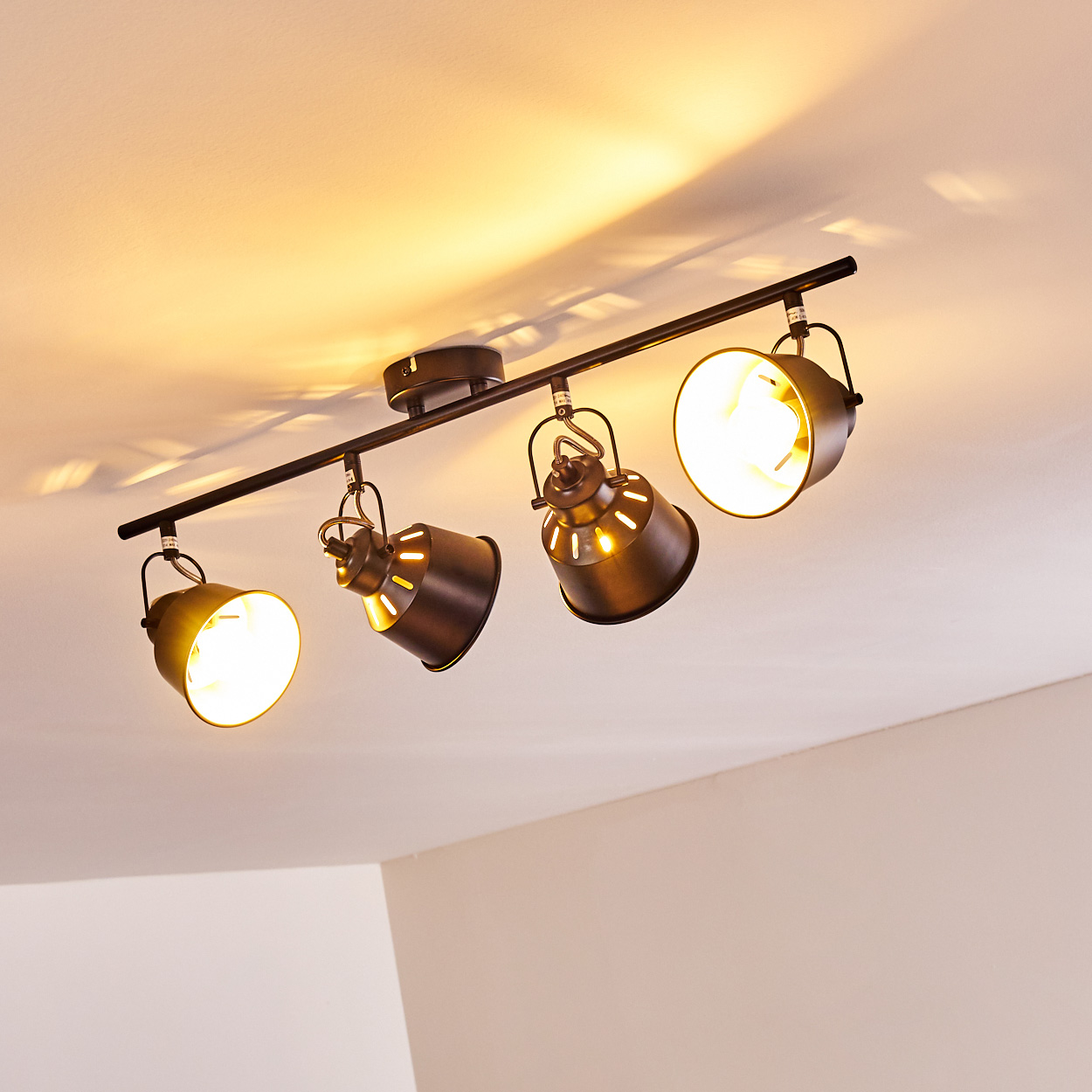 Schwarzer Deckenstrahler mit vier verstellbaren Lampen, die warmes Licht spenden.