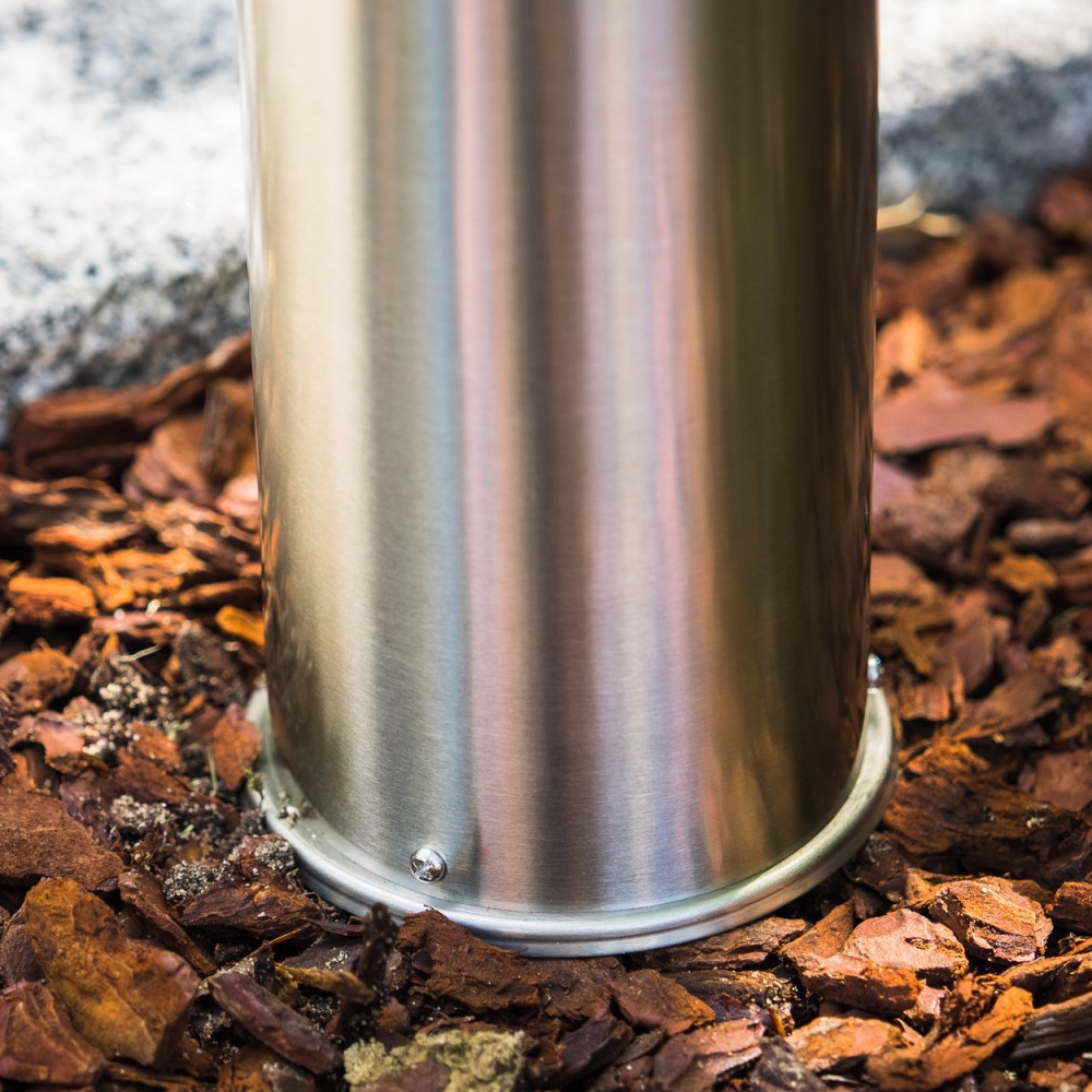 Ein glänzender Metallpfosten steht auf Rindenmulch neben einem Stein.
