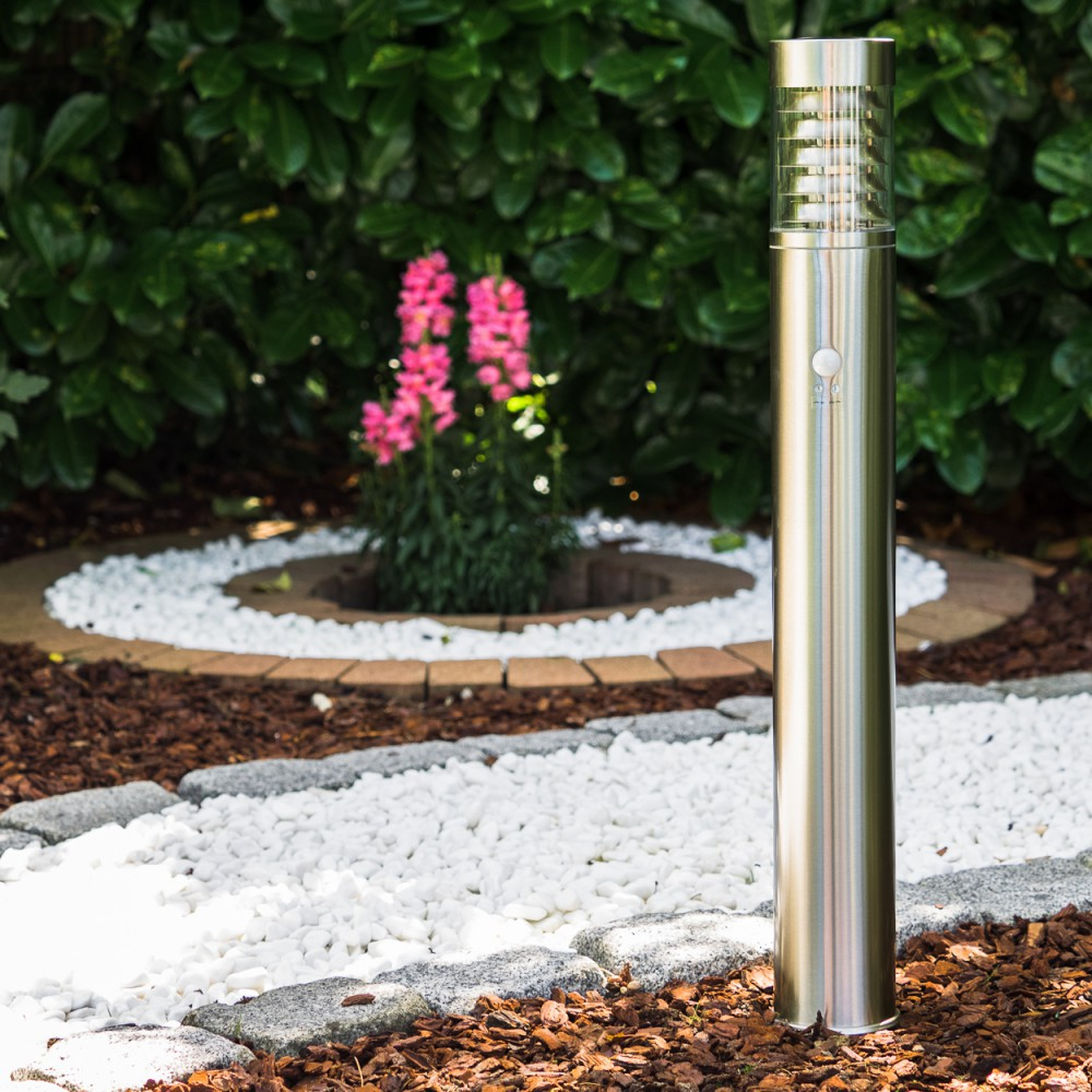 Ein moderner Metallpfosten steht neben rosa Blumen und weißem Kies in einem Garten.