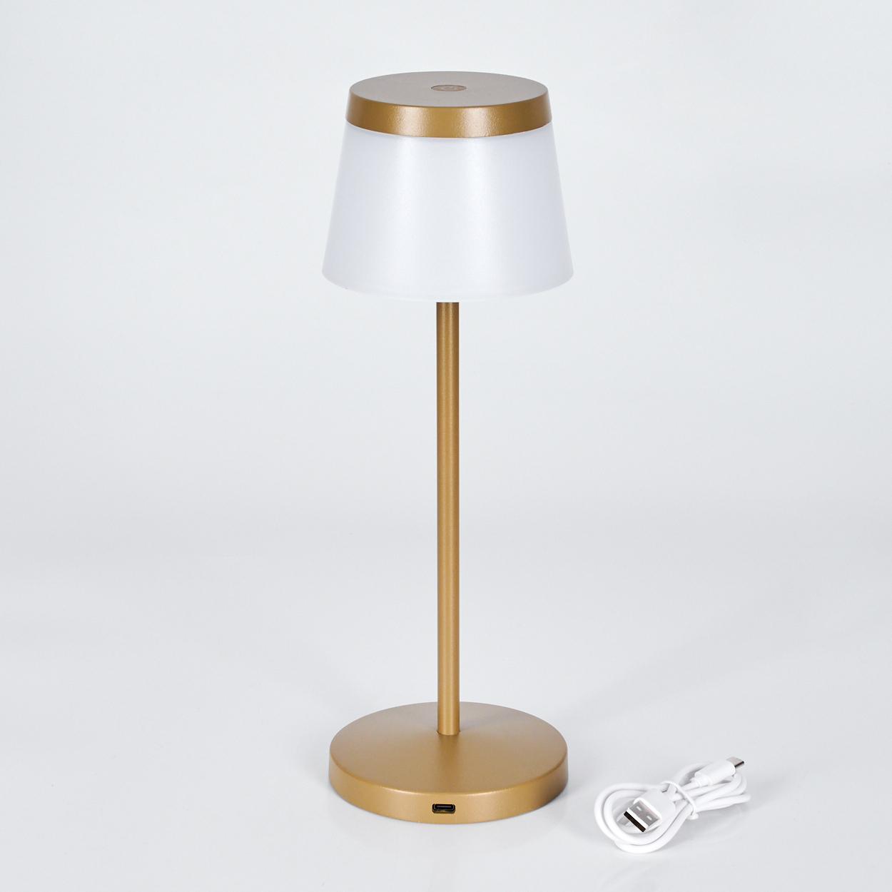 Eine goldene Lampe mit weißem Schirm und USB-Kabel auf weißem Hintergrund.