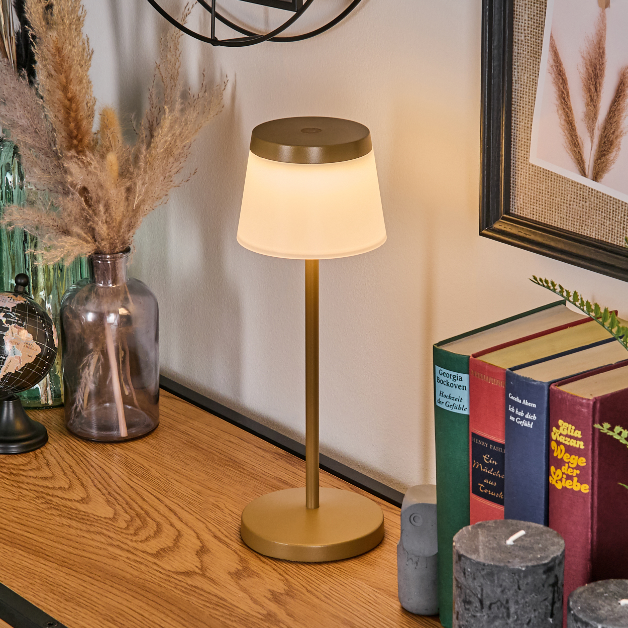 Eine goldene Tischlampe steht auf einem Holztisch neben Büchern und Pflanzen.