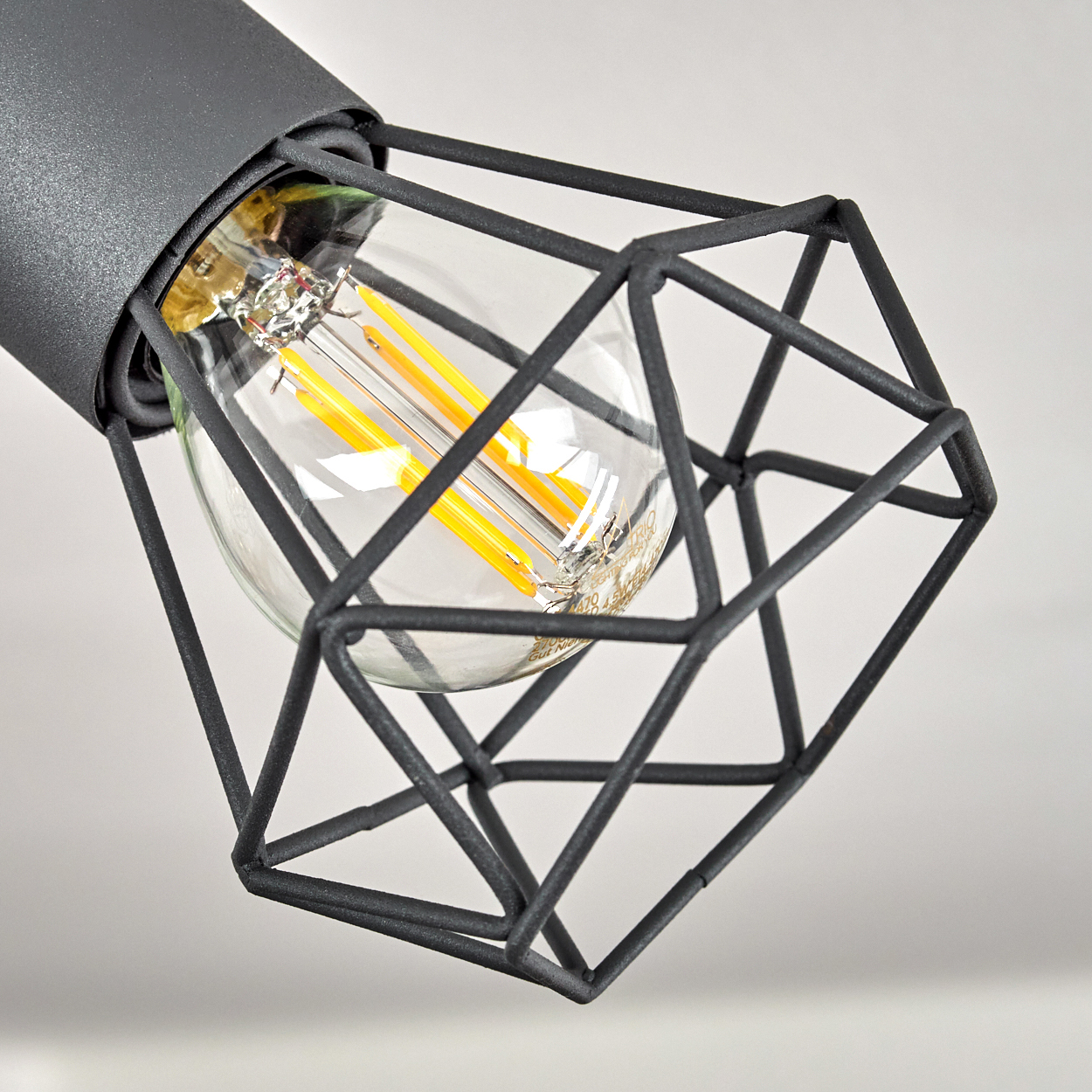 Eine graue Lampe mit einem Drahtkäfig und einer sichtbaren Glühbirne mit gelben Filamenten.