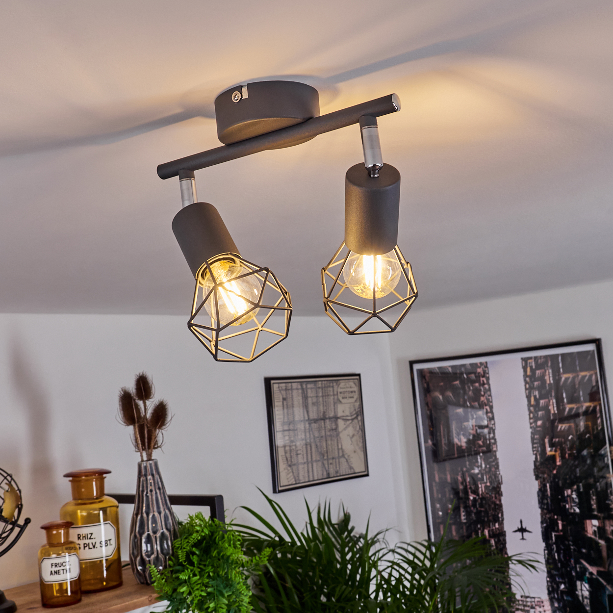 Eine dunkle Deckenlampe mit zwei Lichtquellen und geometrischen Metallkäfigen.