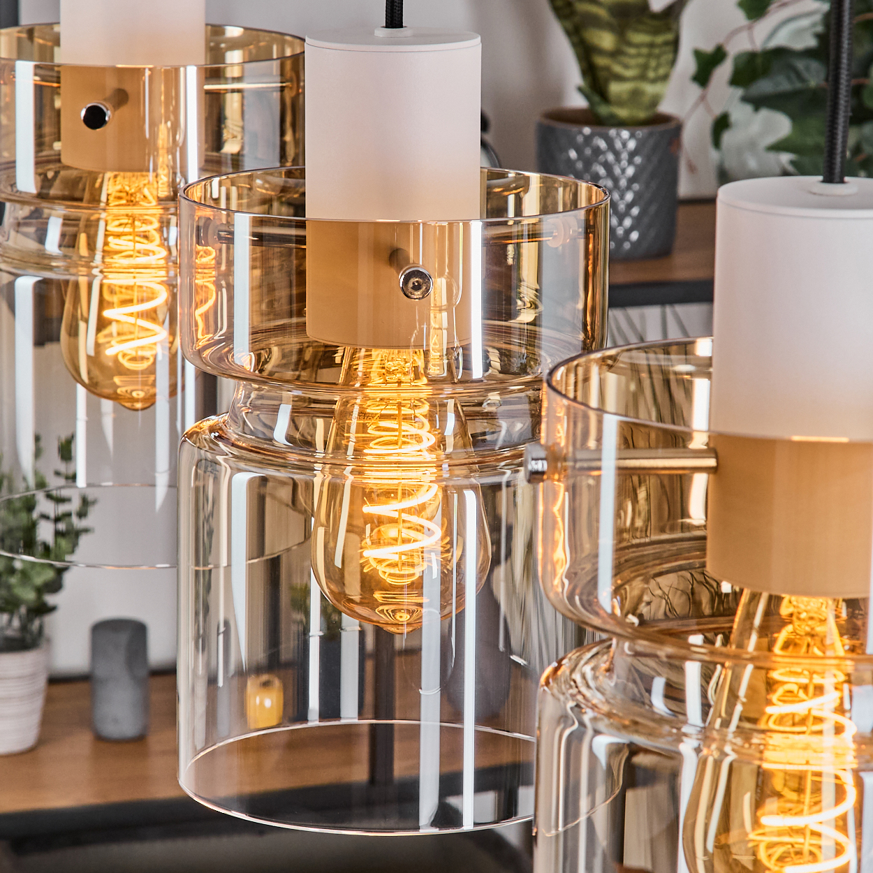 Mehrere Pendelleuchten mit bernsteinfarbenen Glaszylindern und Glühfadenlampen.