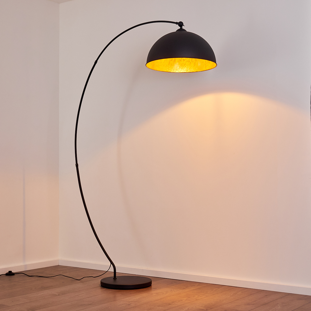 Ein schwarzer Bogenlampenschirm mit goldener Innenseite beleuchtet eine weiße Wand.