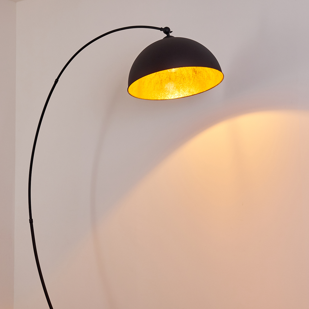 Eine schwarze Bogenlampe mit einem halbrunden Schirm mit goldener Innenseite.