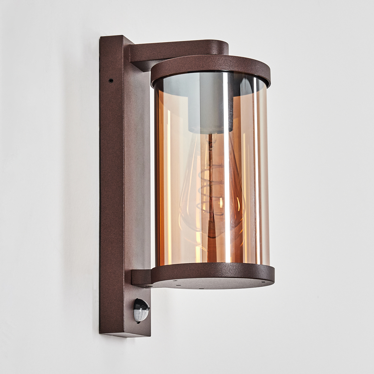 Braune Wandleuchte mit zylindrischem Bernstein-Glas und sichtbarer Glühbirne.