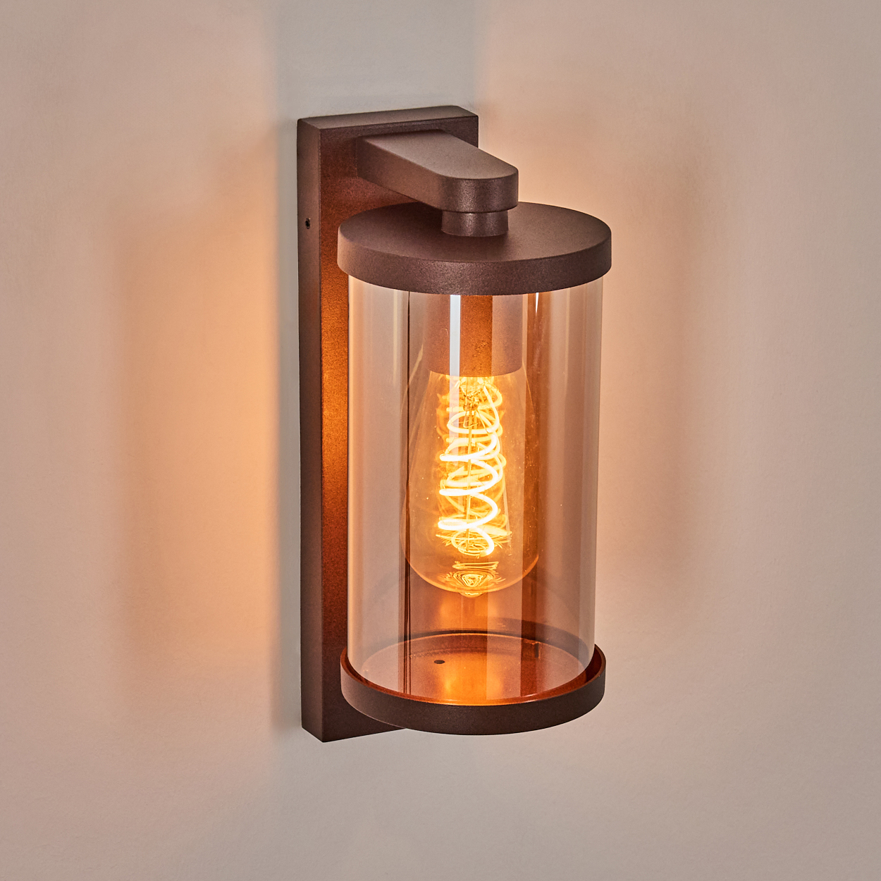 Eine dunkle Wandleuchte mit zylindrischem Glas und sichtbarer Glühbirne.