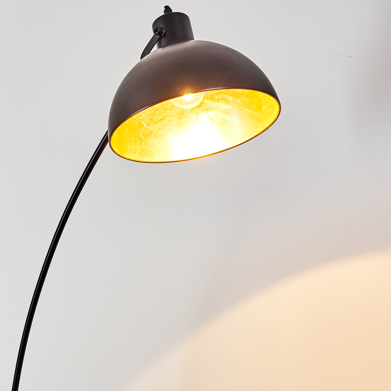 Eine dunkle Stehlampe mit einem Lampenschirm, der golden beleuchtet ist.