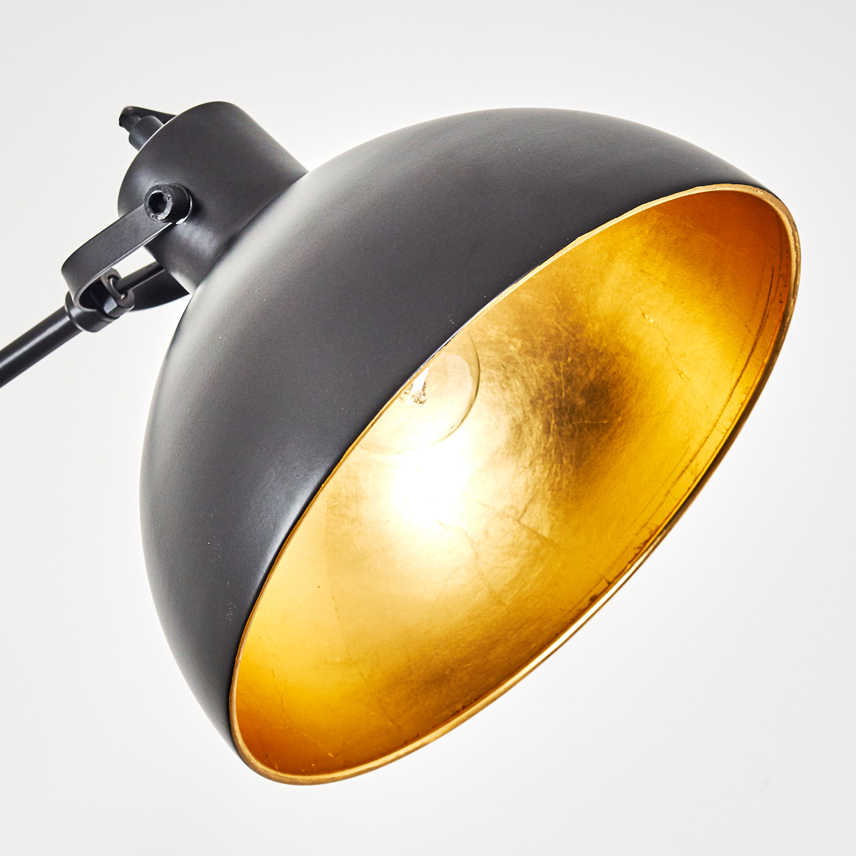 Eine schwarz-goldene Lampe mit einem Lampenschirm, der von innen golden ist.
