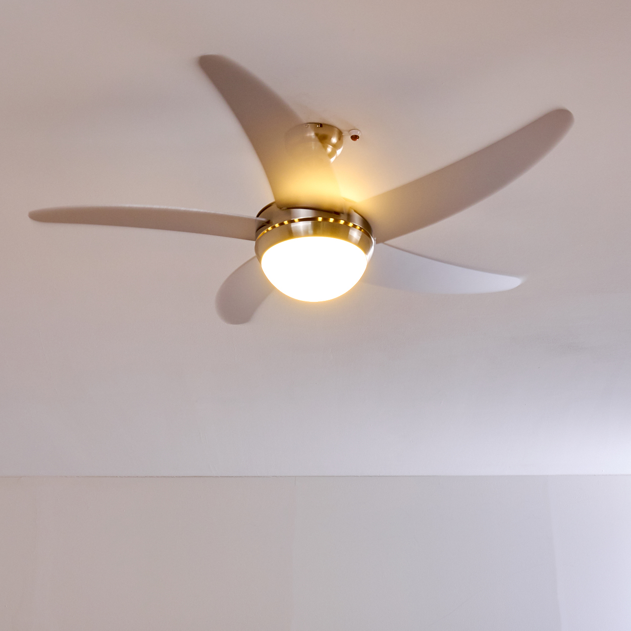 Ein moderner Deckenventilator mit Licht dreht sich über einem weißen Raum.