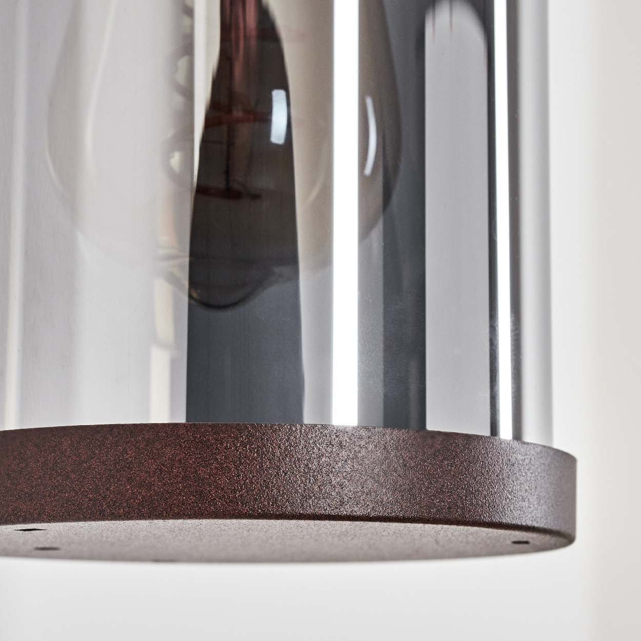 Nahaufnahme einer zylindrischen Lampe mit braunem Sockel und Glaszylinder.