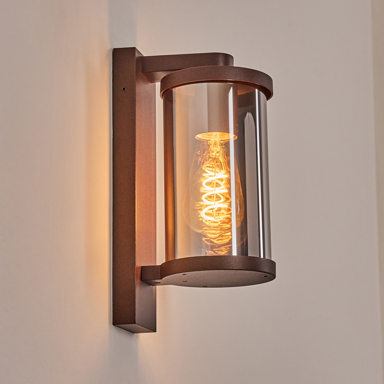 Braune Wandleuchte mit zylindrischem Glas und sichtbarer Glühbirne.