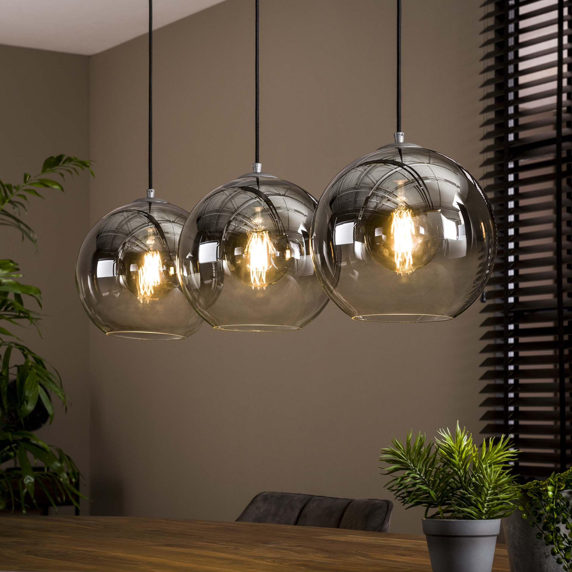 Drei runde, bronzefarbene Pendelleuchten mit sichtbaren Glühbirnen hängen über einem Holztisch.