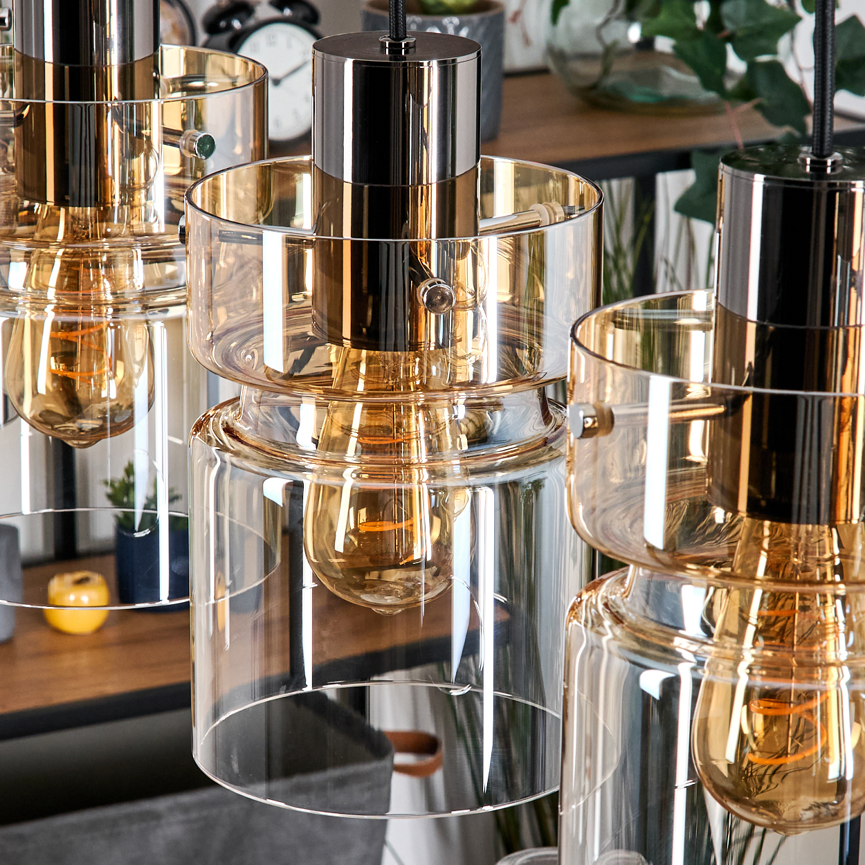 Mehrere moderne Pendelleuchten mit bernsteinfarbenen Glaszylindern und glänzenden Metalloberteilen.