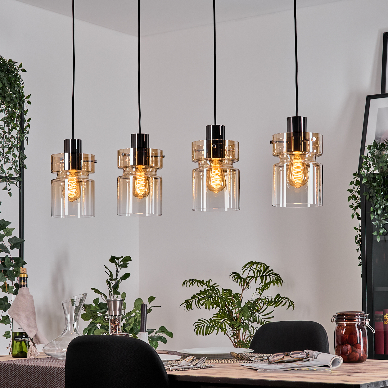 Vier Glaspendelleuchten mit Edison-Glühbirnen hängen über einem Esstisch.
