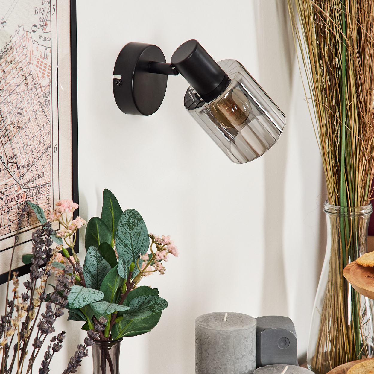 Ein schwarzer Wandspot mit Glaszylinder über einer Karte, Blumen und Kerzen.