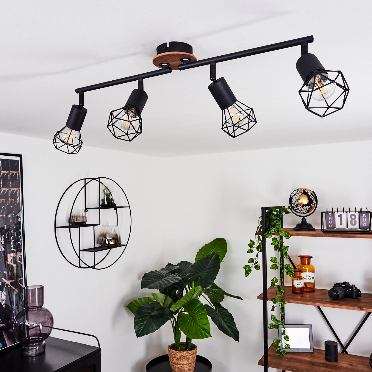 Ein schwarzer Deckenstrahler mit vier Lampen und Gitterschirmen über einem Regal mit Pflanzen und Deko.