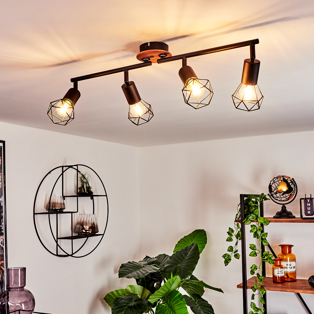 Eine Deckenleuchte mit vier Lampen, schwarzen Metallkäfigen und Holzdetails.