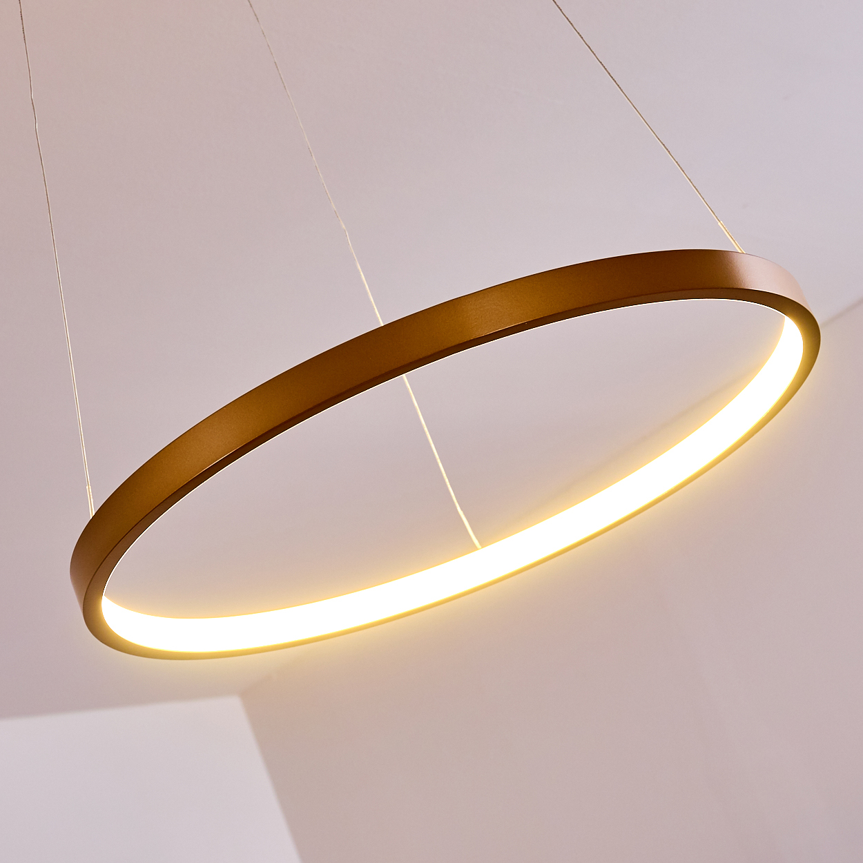 Eine goldene Ringlampe hängt von dünnen Drähten mit hellem Licht.
