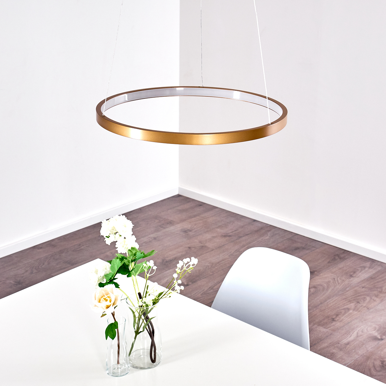 Goldener Ring-Kronleuchter über einem weißen Tisch mit Blumen und einem Stuhl.