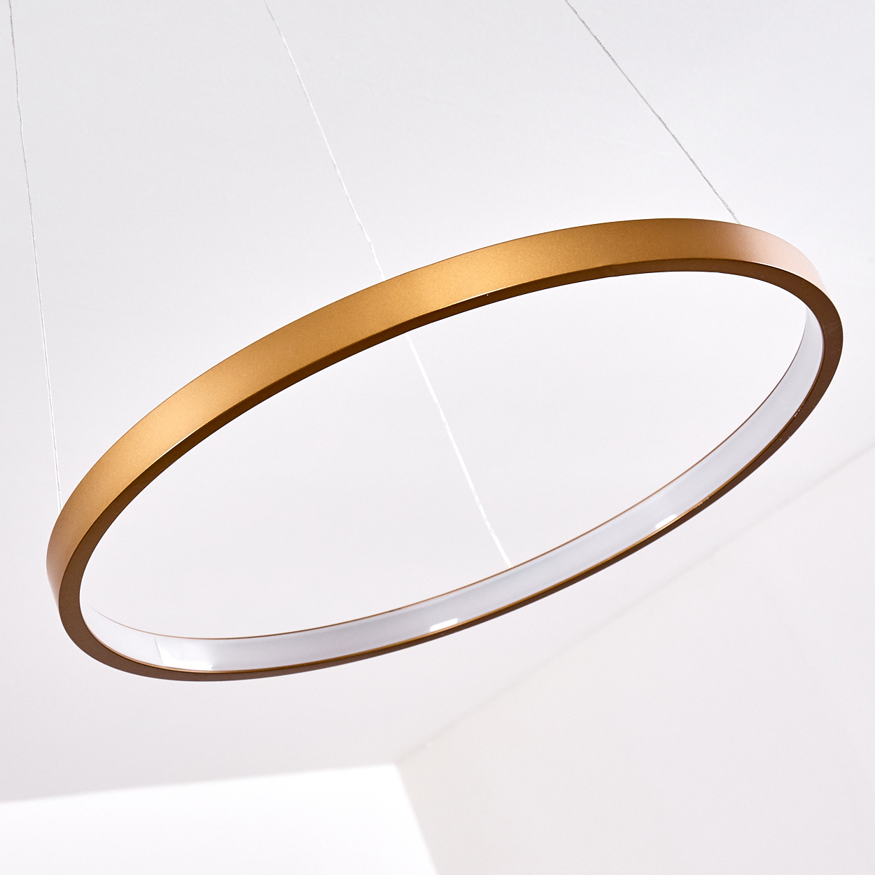 Eine goldene Ringlampe hängt von dünnen Drähten an einer weißen Decke.