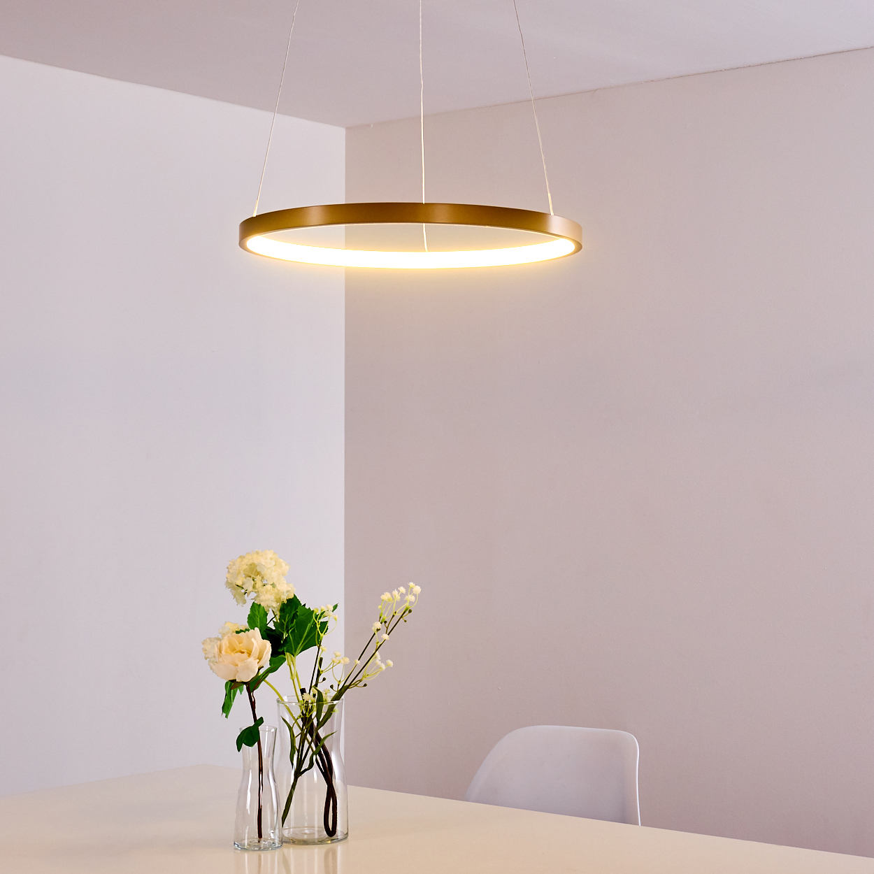 Ein runder goldener Deckenventilator leuchtet über einem Tisch mit Blumen in Gläsern.