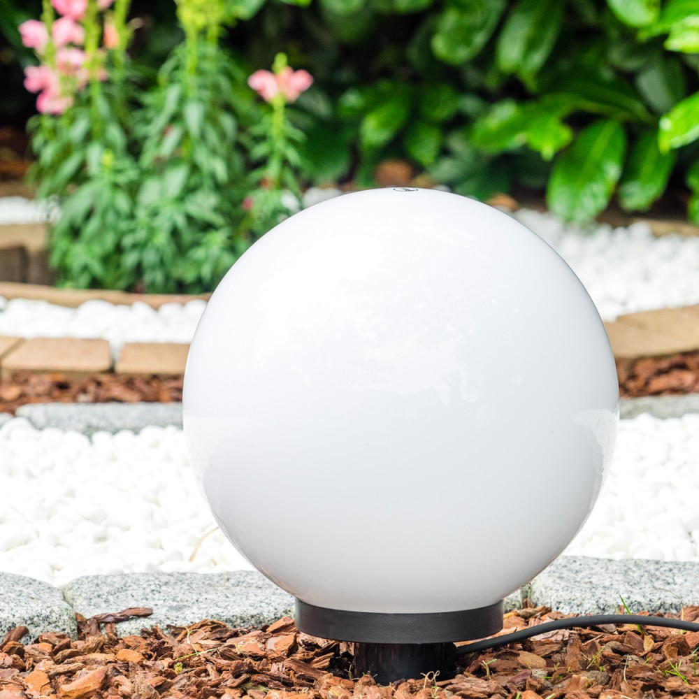 Eine weiße kugelförmige Lampe steht in einem Garten mit Kies und Rinde.