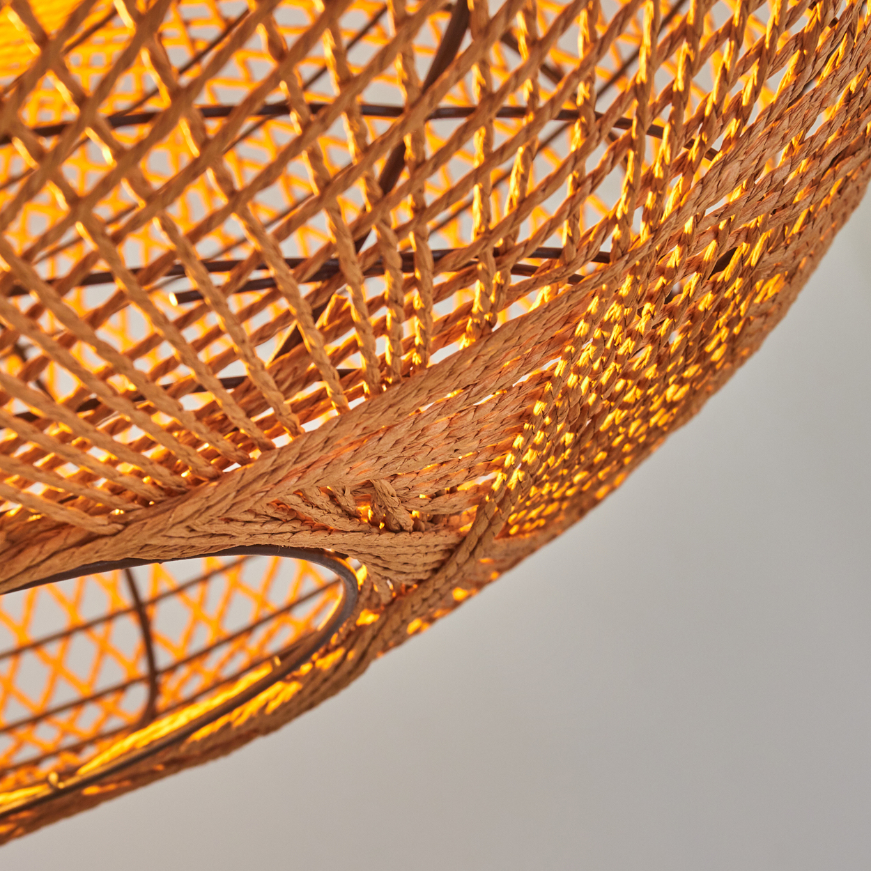 Detailaufnahme einer braunen, geflochtenen Lampe mit warmem Lichtschein.