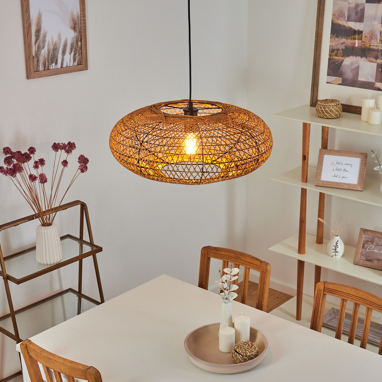 Ein runder Weidenkorb-Pendelleuchter hängt über einem weißen Tisch mit Holzstühlen.