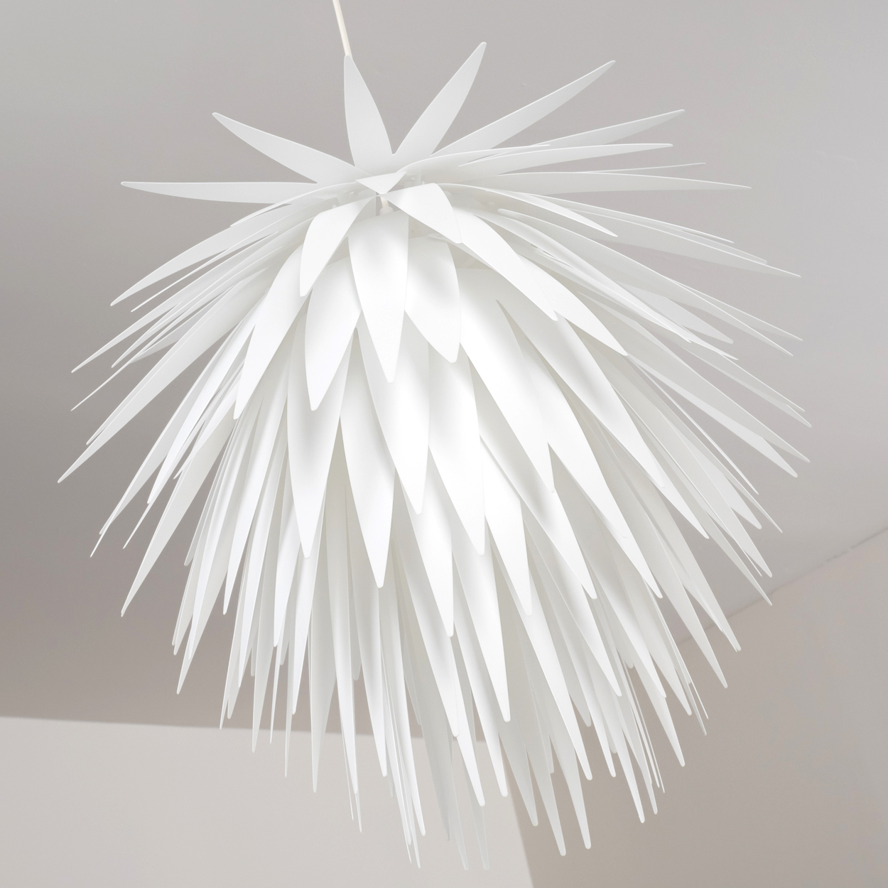 Eine weiße Lampe mit spitzen, überlappenden Elementen hängt von der Decke.