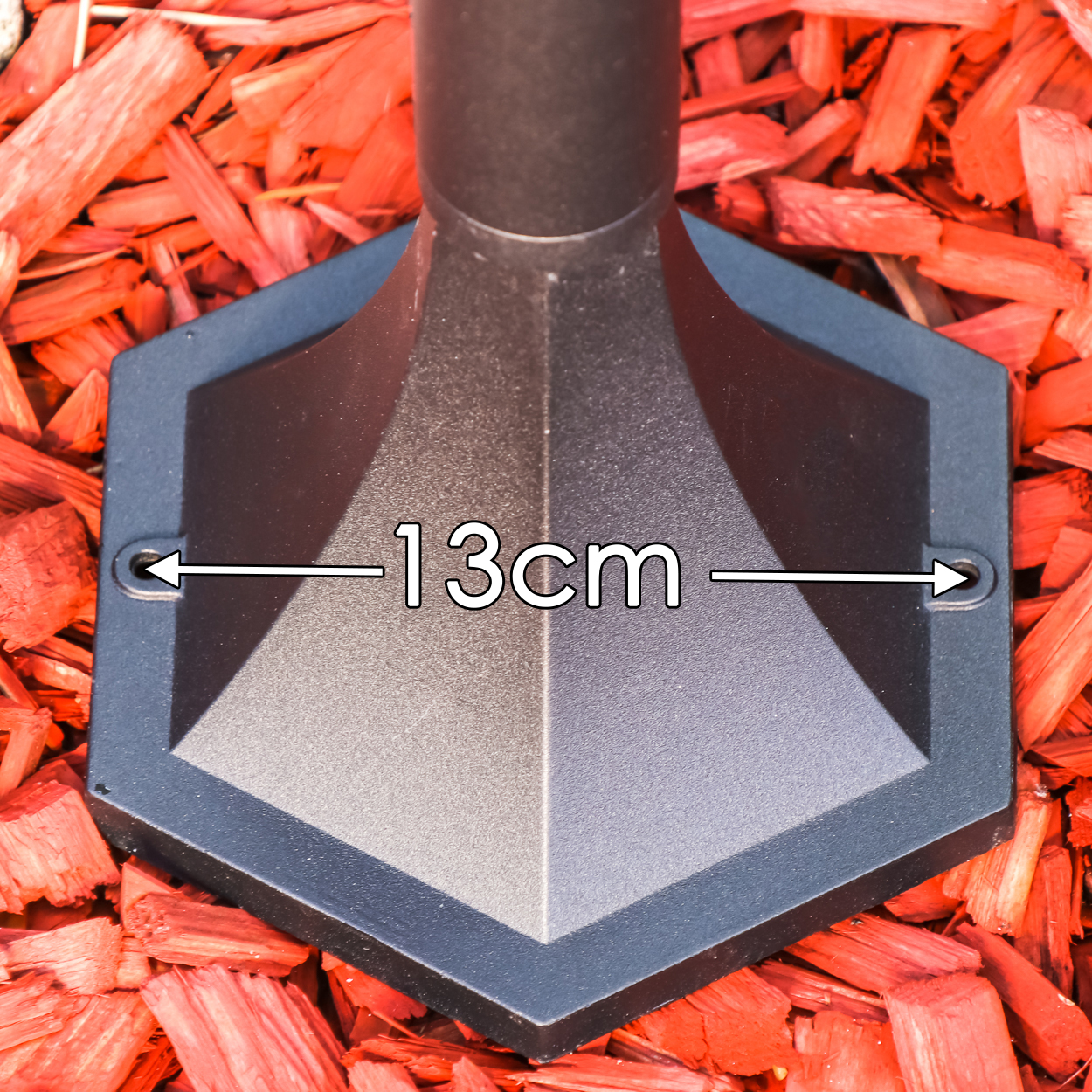 Ein dunkles sechseckiges Objekt mit Maßangabe von 13 cm auf rotem Mulch.