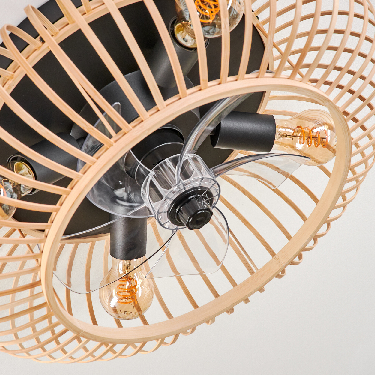 Deckenventilator mit Rattangeflecht, transparenten Rotorblättern und Glühbirnen.