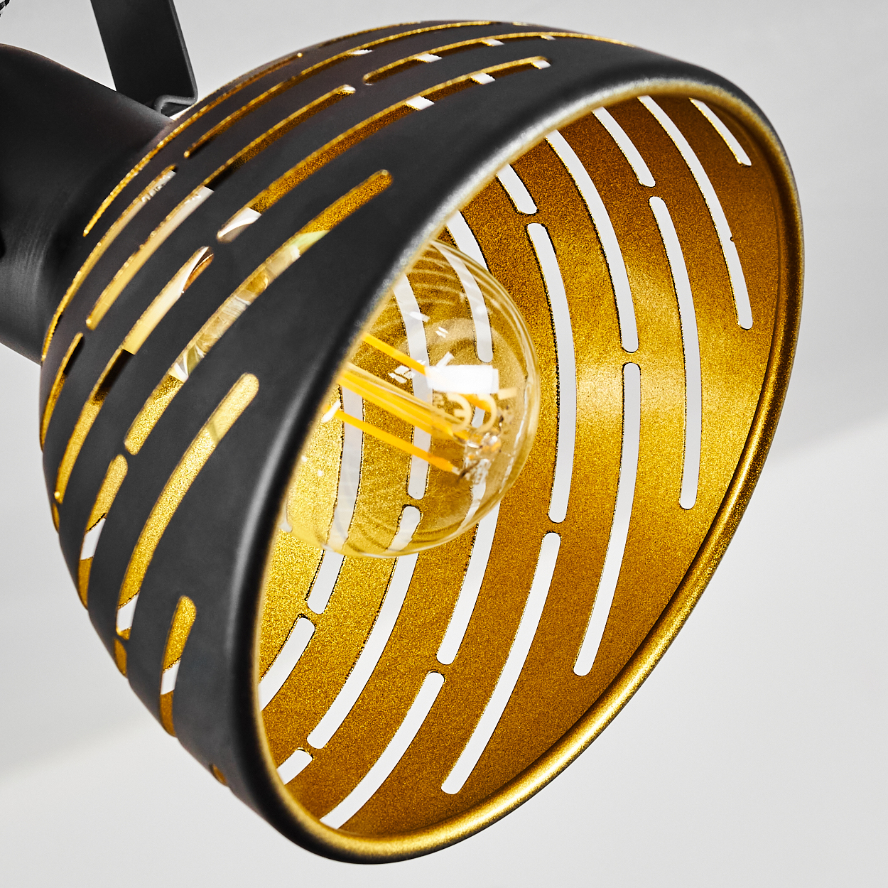 Eine goldene Lampe mit schwarzem Gitter und sichtbarer Glühbirne.