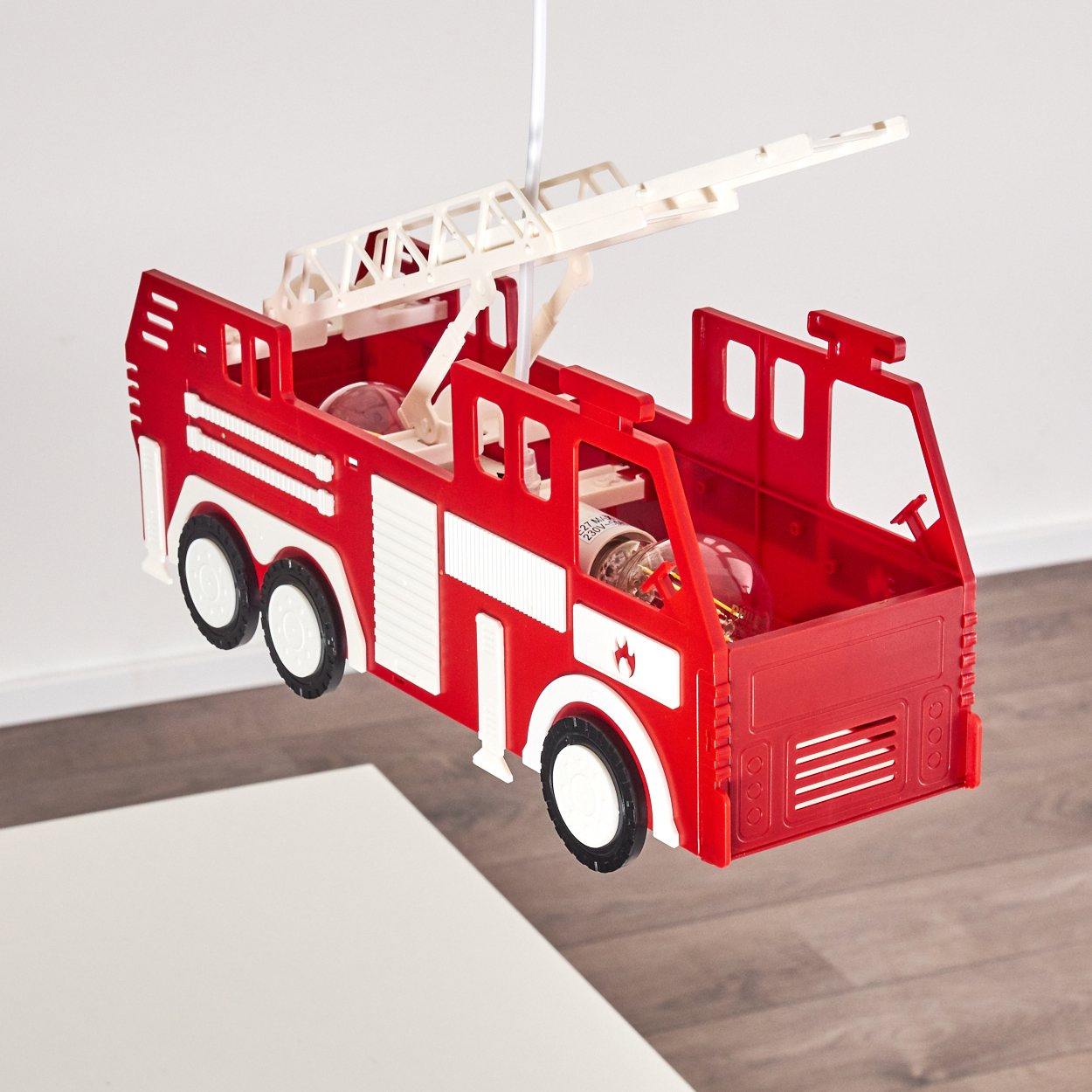 Rotes Spielzeug-Feuerwehrauto mit ausklappbarer Leiter hängt von weißem Kabel.