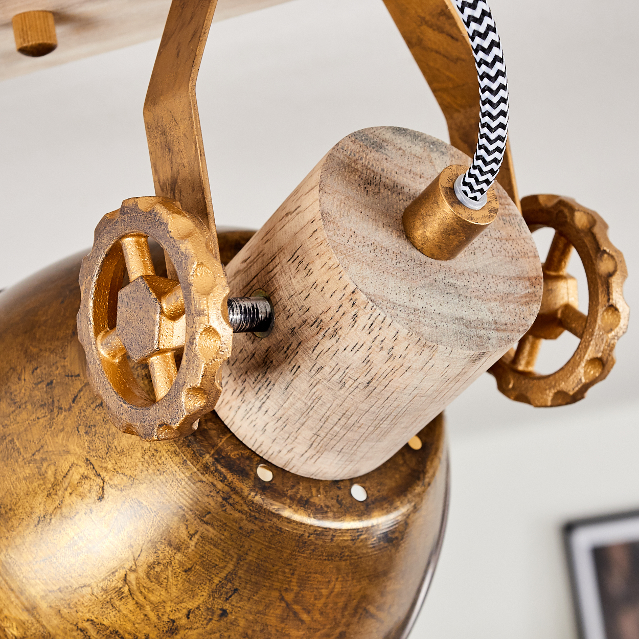 Detail einer goldenen Lampe mit Holz- und Zahnradelementen, schwarz-weißer Kabel.