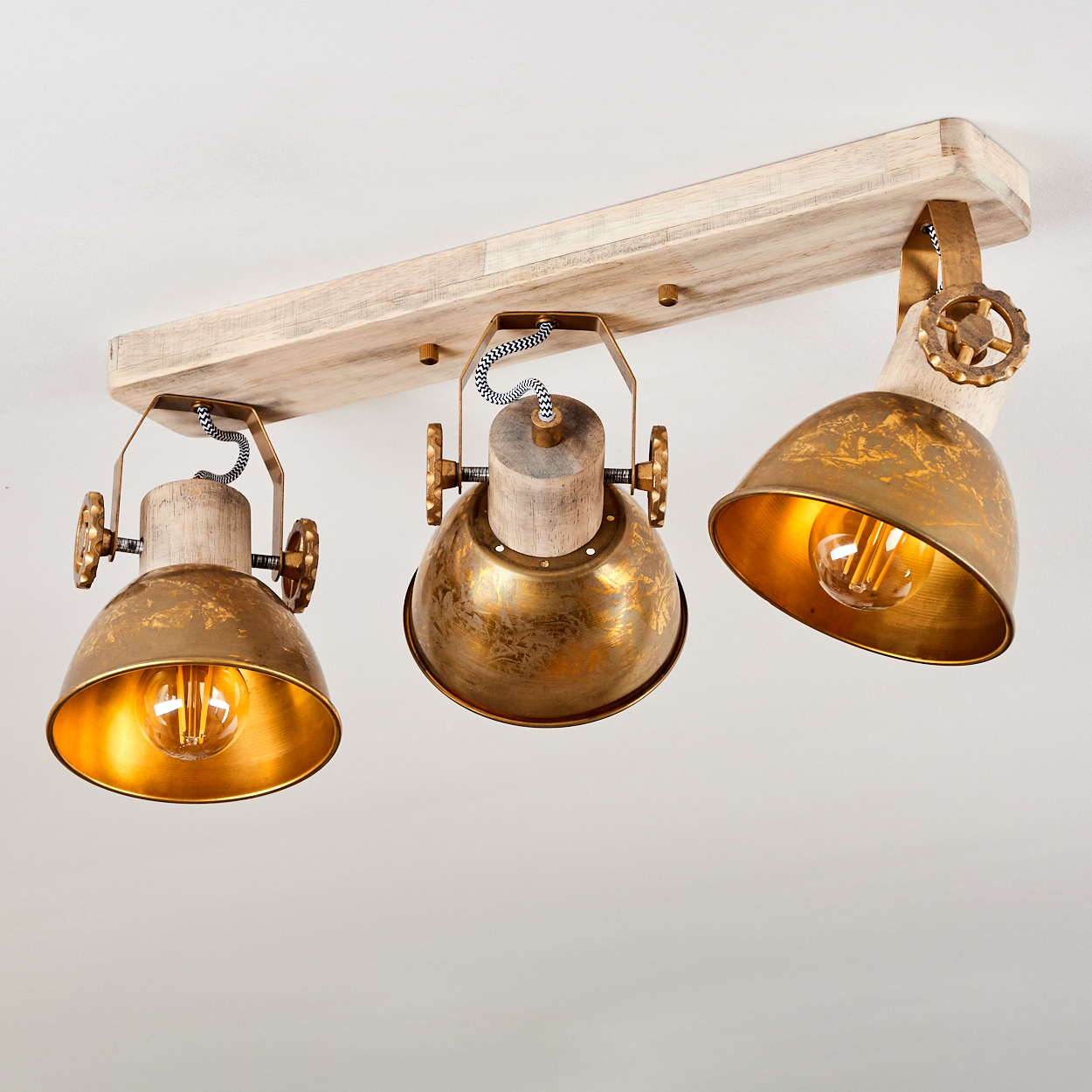 Eine Holzleiste mit drei goldenen Lampenschirmen und sichtbaren Glühbirnen.