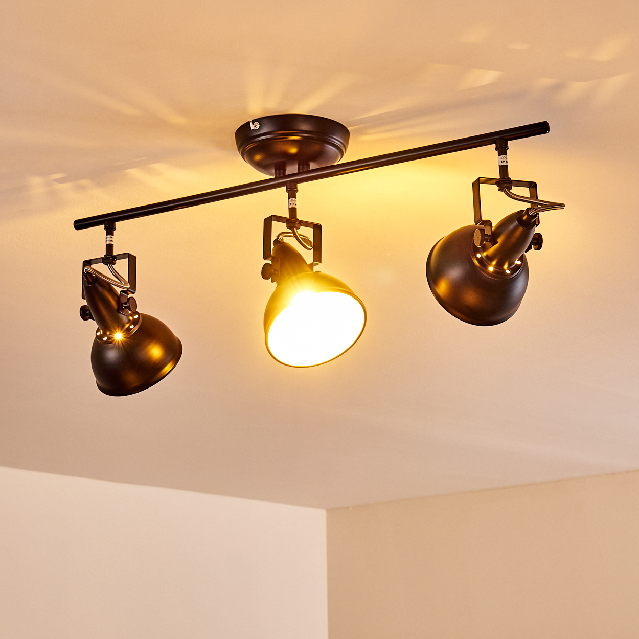 Eine schwarze Schienenleuchte mit drei verstellbaren Lampen ist an einer weißen Decke montiert.