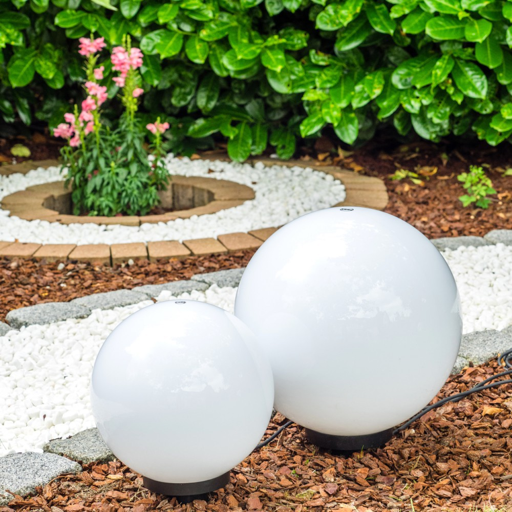 Zwei weiße Kugelleuchten im Garten, umgeben von Kies und Rindenmulch.