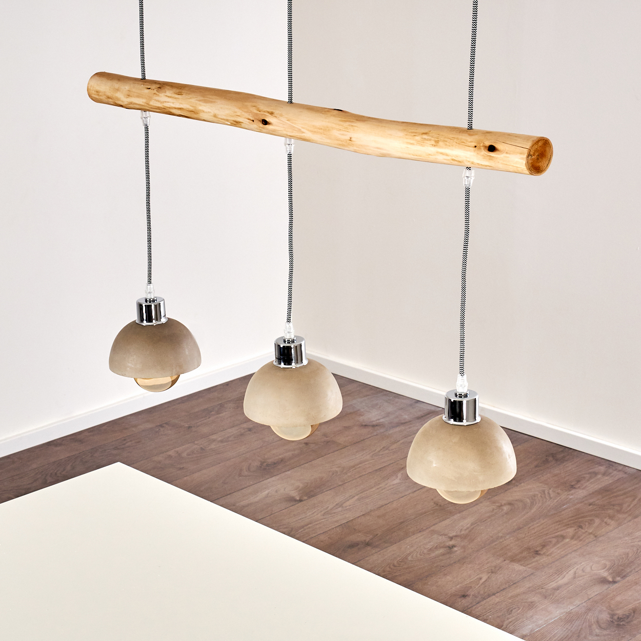 Eine Hängelampe mit drei Lampenschirmen aus Beton, die an einem Holzstamm befestigt sind.