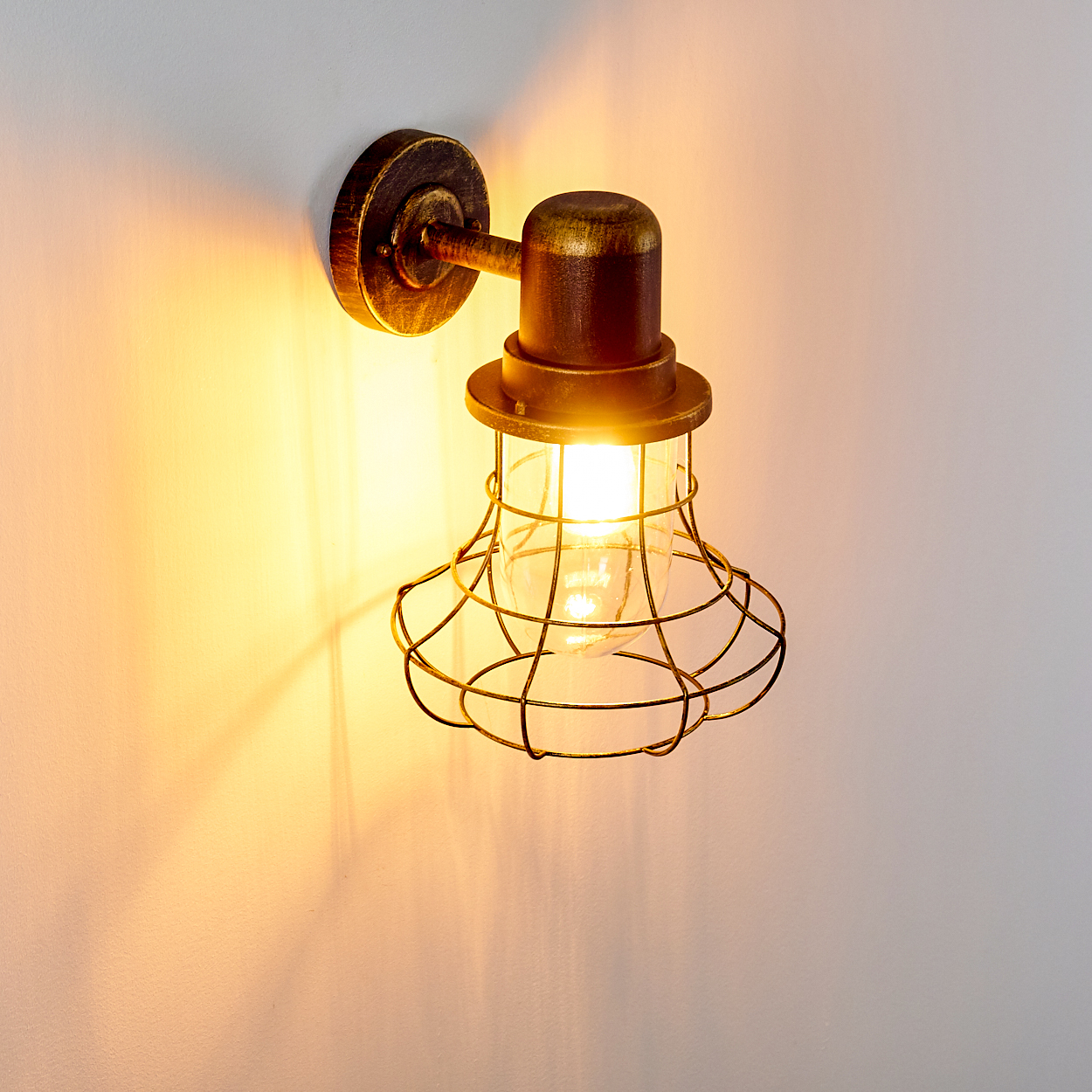 Eine Wandleuchte mit einem Drahtgitter-Lampenschirm leuchtet warmes Licht.