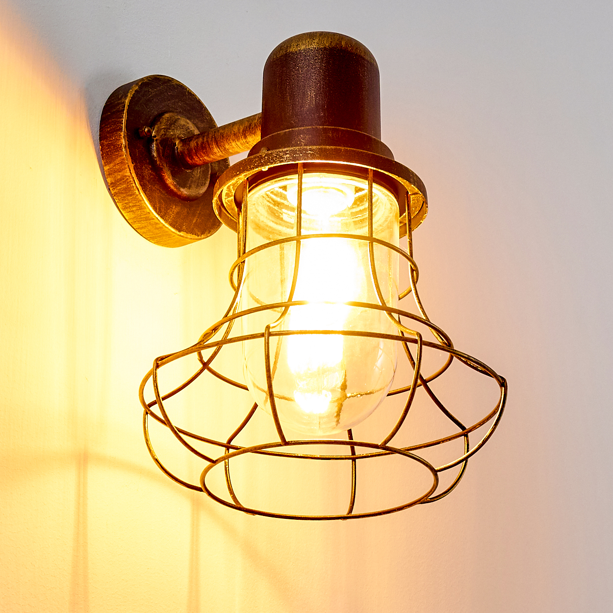 Eine antike Wandleuchte mit Glaskolben und Metallkäfig, die warmes Licht spendet.