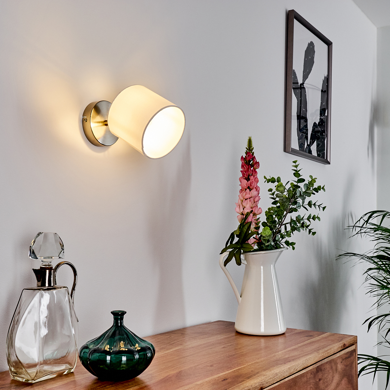 Ein Wandleuchter beleuchtet eine Wand über einem Holzmöbel mit Vasen und Pflanzen.