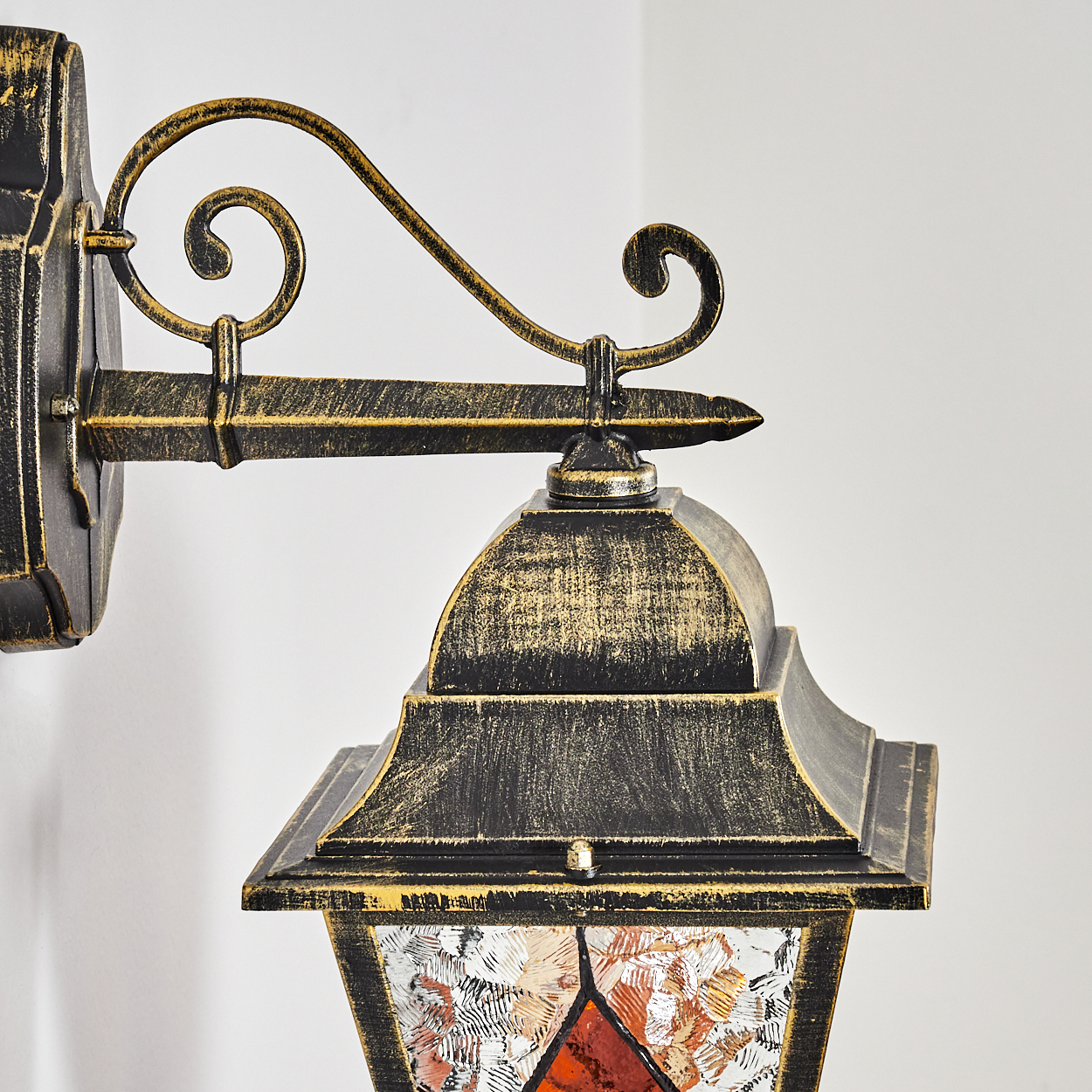 Eine goldene Wandlampe mit Verzierungen und bunten Glasfenstern.