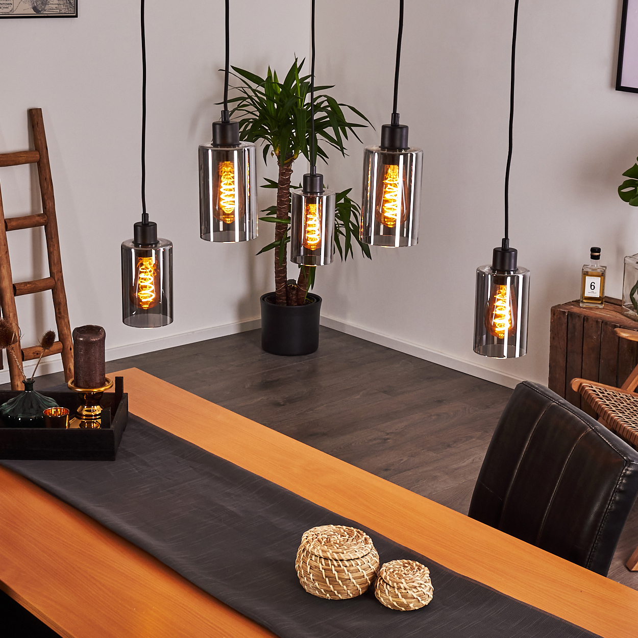 Fünf Pendelleuchten mit Glaszylindern und sichtbaren Glühbirnen über einem Holztisch.