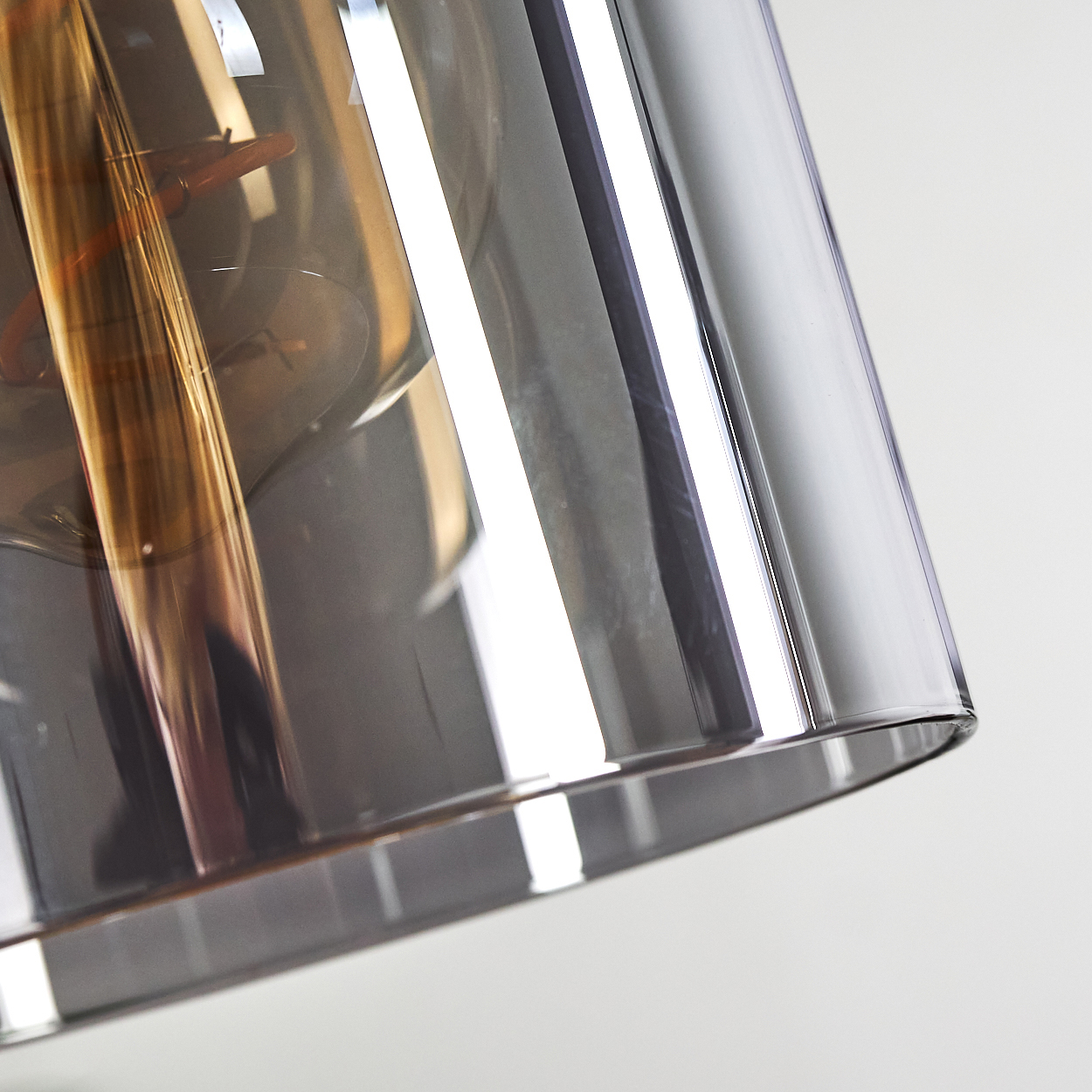 Nahaufnahme einer rauchfarbenen Glaslampe mit sichtbarem Glühfaden, reflektierendem Licht.
