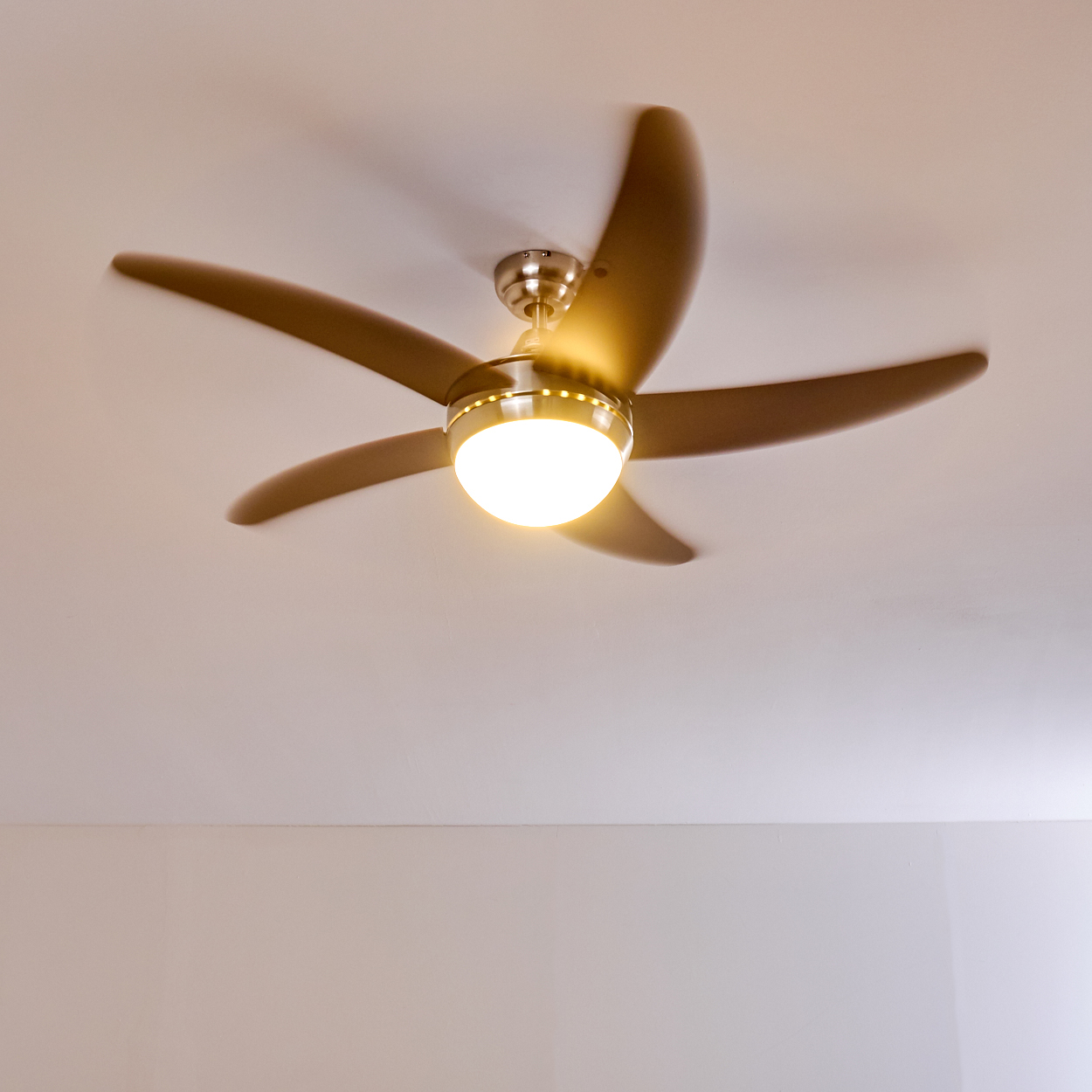 Ein Deckenventilator mit fünf braunen Flügeln und einer runden Lampe dreht sich.