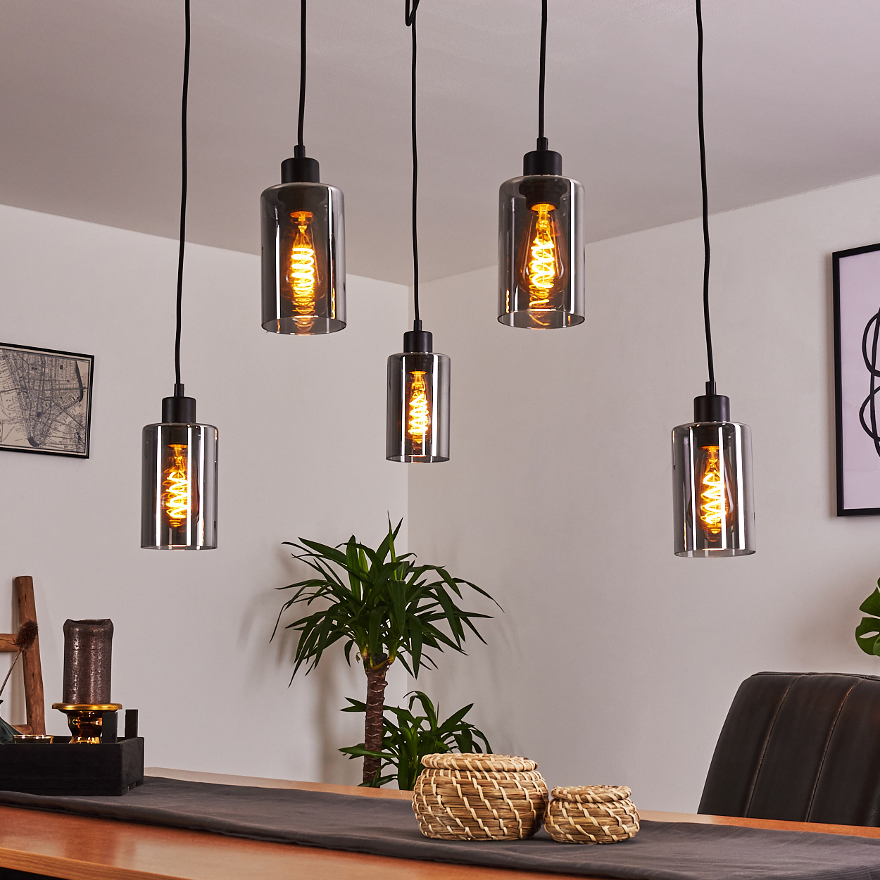 Fünf zylindrische Pendelleuchten mit Edison-Glühbirnen hängen über einem Holztisch.