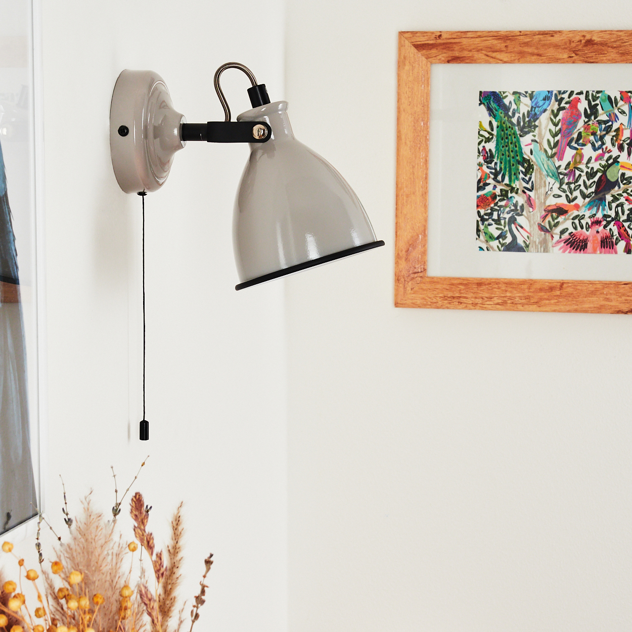 Graue Wandlampe mit Zugschalter neben einem Bild mit bunten Vögeln.